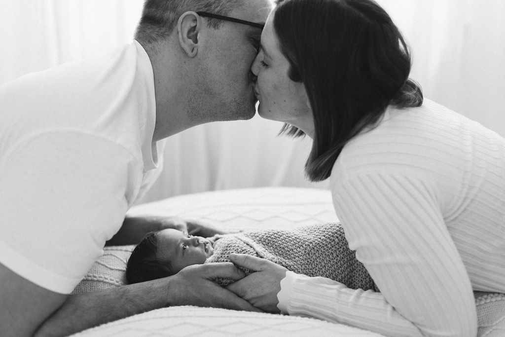 papa und mama küssen sich baby schaut neugeborenenbilder im studio